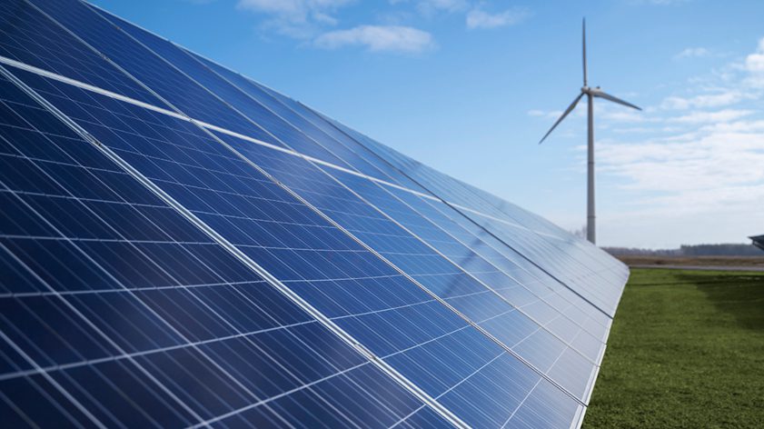 Solar panels and a wind turbine in a green field under a sunny blue sky