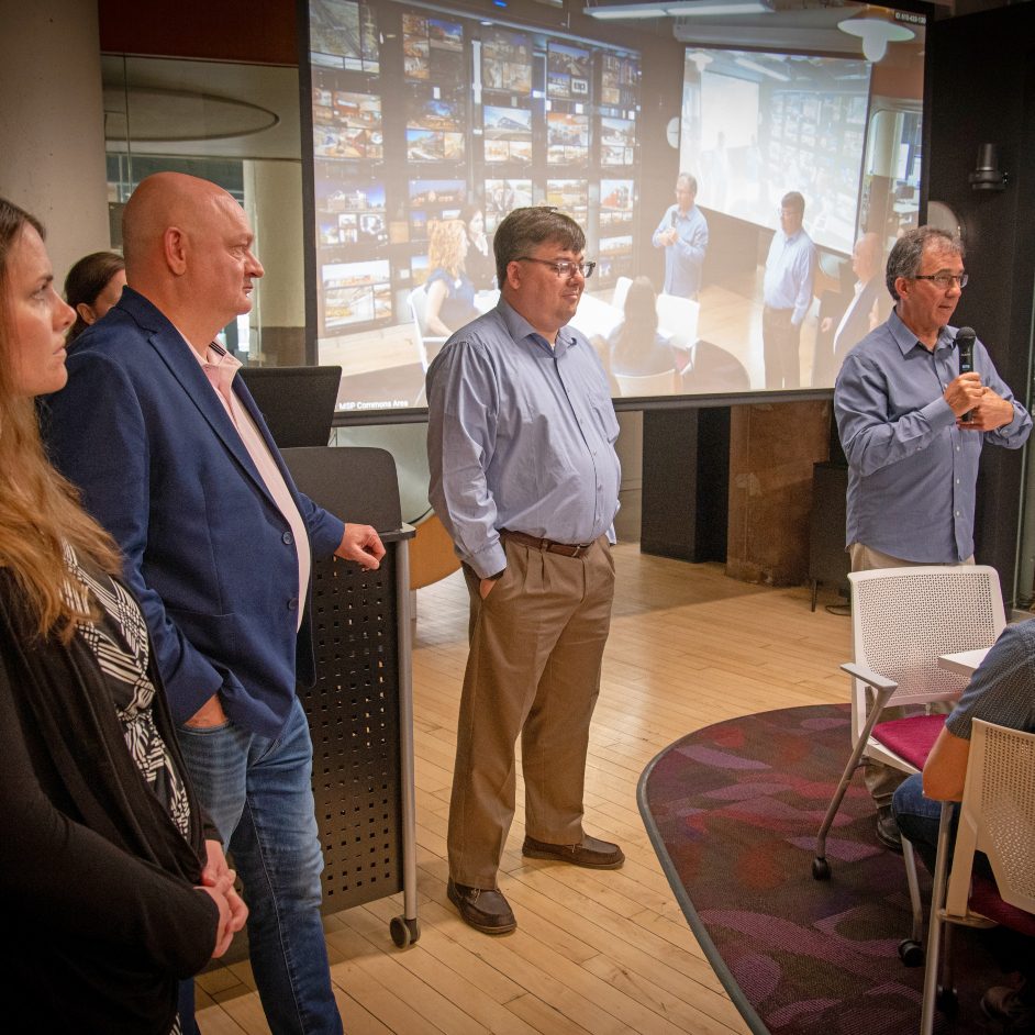 Four people in front of a video screen doing a presentation